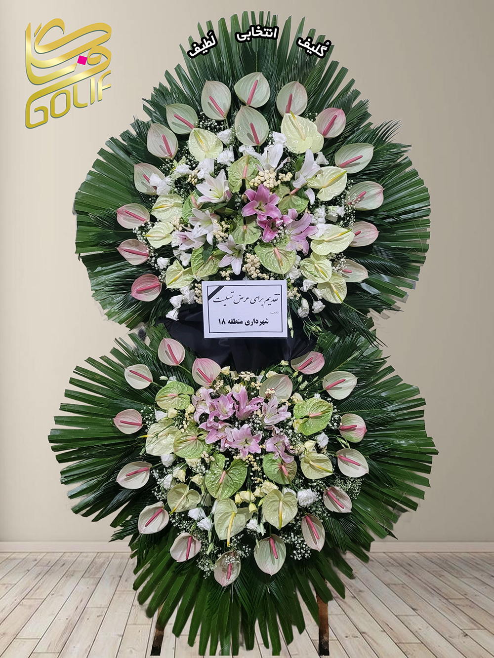 تاج گل تبریک دو طبقه گل‌های اصلی و غالب این تاج گل به شرح زیر هستند: - **آنتوریوم سفید و صورتی:** این گل‌ها با اسپات‌های چشم‌نواز در طراحی مرکزی تاج گل برجسته هستند. - **رز سفید:** در قسمت‌های مختلف تاج گل دیده می‌شوند که زیبایی و طراوت خاصی ایجاد کرده‌اند. - **لیلیوم صورتی و سفید:** این گل‌ها هم در ترکیب برجسته تاج گل حضور دارند و جلوه‌ای لوکس به آن بخشیده‌اند. این ترکیب گل‌ها به همراه متن تسلیت، نمایانگر احترام و همدردی است. تاج گل افتتاحیه، تاج گل نمایشگاهی، تاج گل عقد و عروسی سفارش آنلاین تاج گل