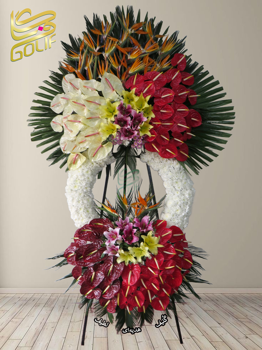 تاج گل تبریک دو طبقه گل‌های اصلی و غالب تاج گل عبارتند از: - **آنتوریوم قرمز و سفید:** این گل‌ها به شکل چشم‌گیری در بالای تاج و سایر بخش‌ها مشاهده می‌شوند. - **لیلیوم زرد:** این گل‌ها در بخش‌های مرکزی و پایینی ترکیب به عنوان گل‌های اصلی برجسته هستند. - **پرنده بهشتی نارنجی و بنفش:** این گل‌ها در قسمت بالای تاج گل ظاهر بسیار زیبایی دارند. ترکیب این گل‌ها به همراه چیدمان چندلایه‌ای، جلوه خاصی به این تاج گل داده است. تاج گل افتتاحیه، تاج گل نمایشگاهی، تاج گل عقد و عروسی سفارش آنلاین تاج گل